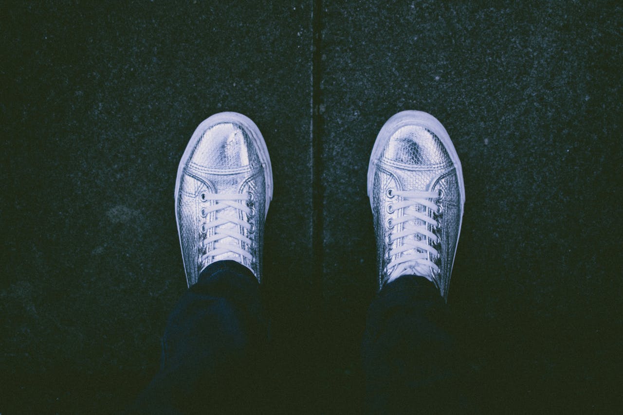 A top view of silver sneakers on a dark pavement background.